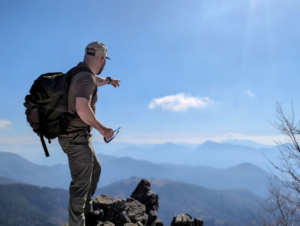 Daniele Mele wijst vanaf een bergtop naar de horizon, tijdens een Cima del BenEssere trail in de Italiaanse Alpen